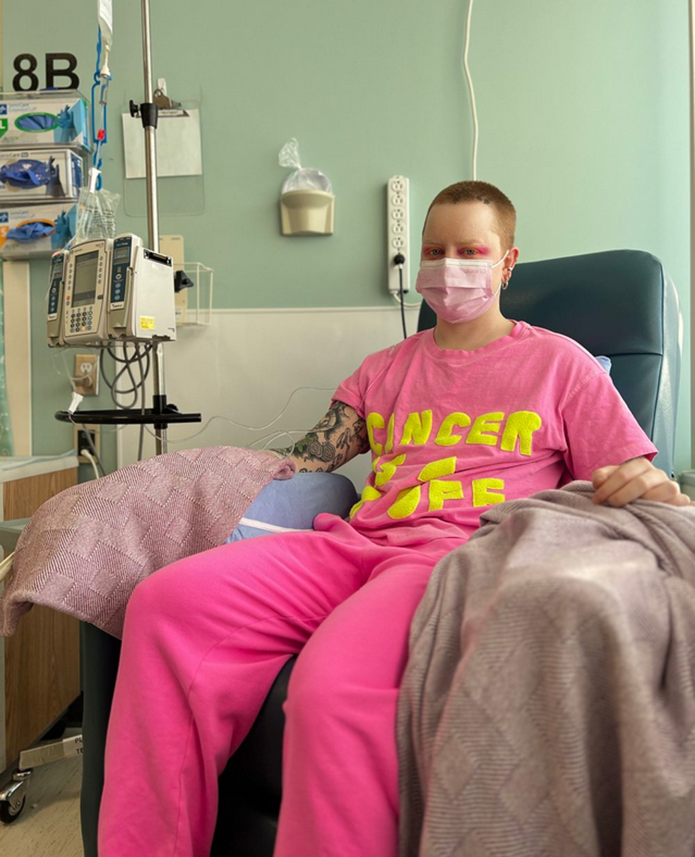 A masked Mike Hooves sits in a chemo chair, bright and defiant in pink