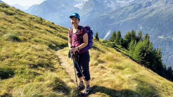 A woman smiling in hiking gear with a beautiful mountain behind her.