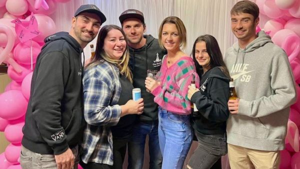 A group of young adults gathered for a photo in front of a white sheet with pink balloons all around.