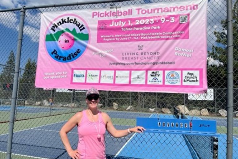 A woman smiling under a pink sign that says "Pickleball Tournament."