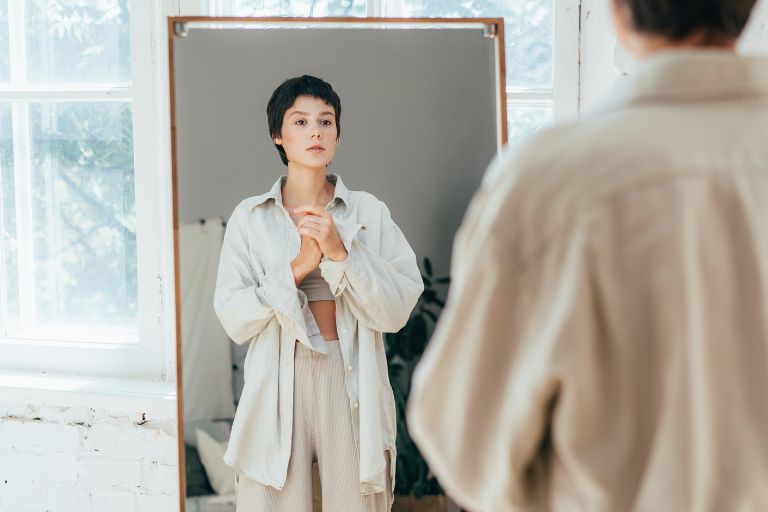 A woman with short hair looks at herself in a mirror