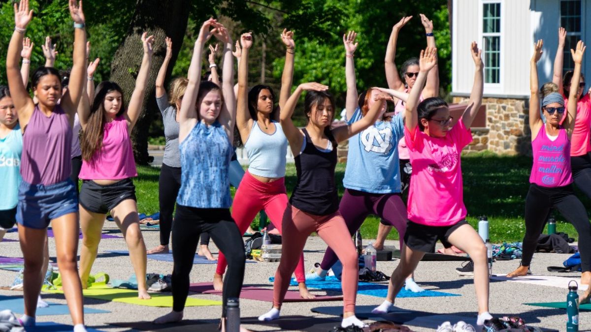 A large group of young women and girls doing yoga outside.