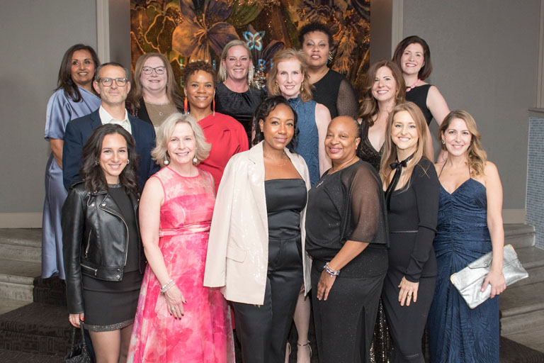 A diverse group of men and women dressed up and smiling on steps at the Butterfly ball.