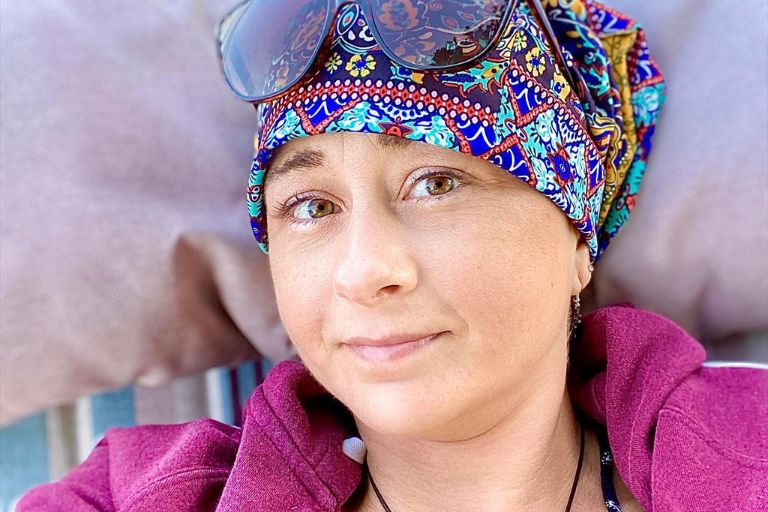 Jenna Antonelli wears sunglasses atop a colorful beanie as she rests mindfully.