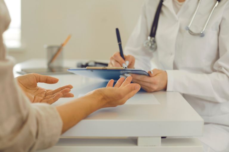 Hands are outstretched in front at a doctor's desk, asking for help.