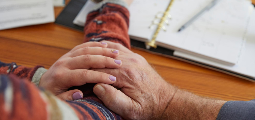 Hands of two people reassuring each other next to paperwork
